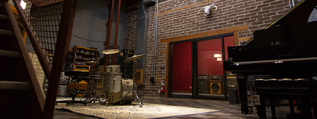 A live room at Electrical Audio — drum kit on a rug, brick walls, red double doors, and a grand piano